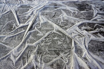 Weiße Eis bedeckte ausgelegte Plastikfolie mit Faltenmuster über grauen Asphaltboden bei Frost, Eis und Schnee am Mittag im Winter