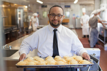 African American man with Down Syndrome as a chef holding a tray of cookies in commercial kitchen