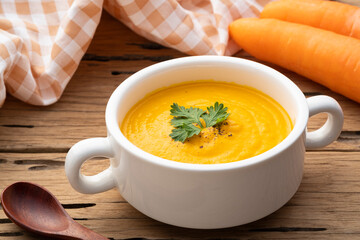 Bowl of tasty Creamy Carrot Soup with vegetables on wooden table,Healthy food