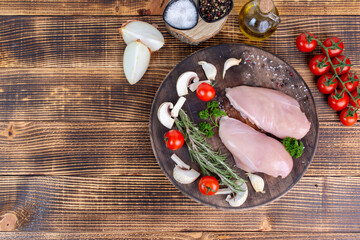 Raw chicken breast fillet with rosemary and spices on a wooden background. Top view. Free space for text or logo