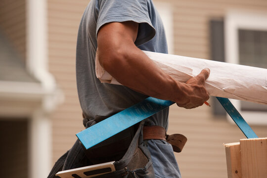 Mid section view of a carpenter carrying a steel square and a blueprint