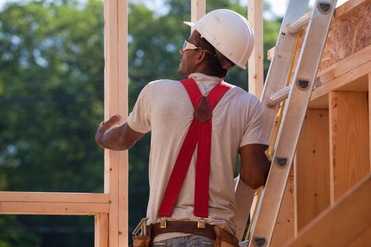 Hispanic carpenter on a ladder checking the framing of a house under construction