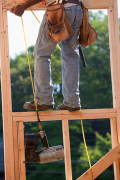 Carpenter pulling nail gun up to the second floor of a house under construction