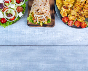 Traditional Greek cuisine concept. Greek food served with Greek salad, chicken souvlaki and gyro pita, top view.  Copy space for text or logo.