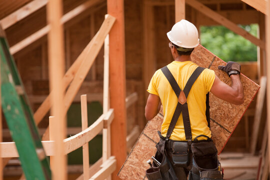 Hispanic carpenter holding a roof panel at a house under construction