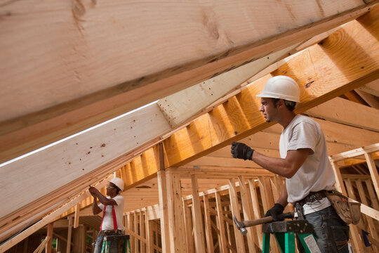 Hispanic carpenters working on roof rafters at a house under construction
