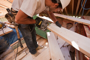 Hispanic carpenter using a circular saw at a  rafter at an angle house under construction