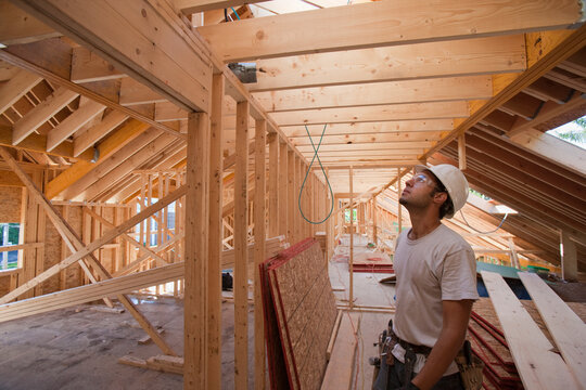 Hispanic carpenter looking at roof on upper floor at a house under construction