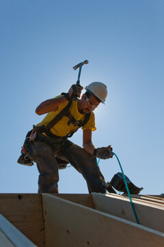 Hispanic carpenter using a hammer on the rafter on roof at a house under construction