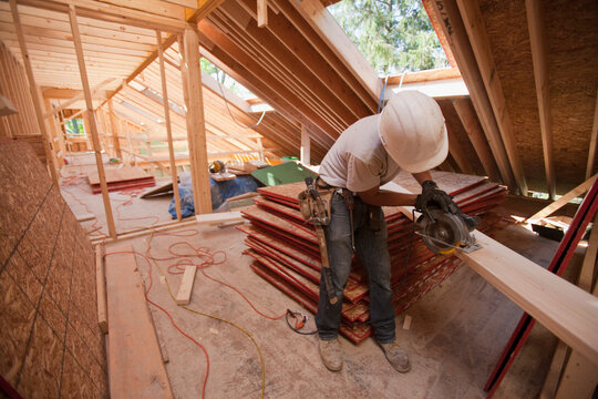 Carpenter using a circular saw on the roof rafter at a house under construction