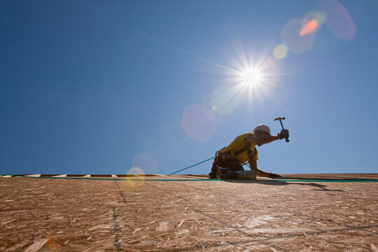 Hispanic carpenter using a hammer on the roofing at a house under construction
