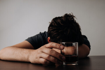 Alcoholism, depressed man sleep on table while drinking alcoholic beverage, holding glass of whiskey - obrazy, fototapety, plakaty