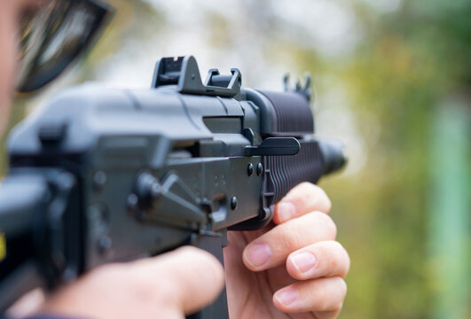 Man takes aim from an assault rifle side view close-up against the background of the forest