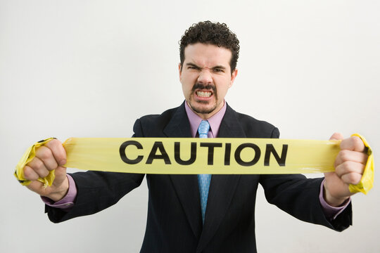 Portrait of a businessman holding a Caution tape and clenching his teeth