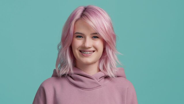 Young playful hipster woman flirting looking straight at camera. Portrait girl with piercing and teeth brackets. Slow motion close up cool funky girl with trendy pastel pink hair color showing tongue