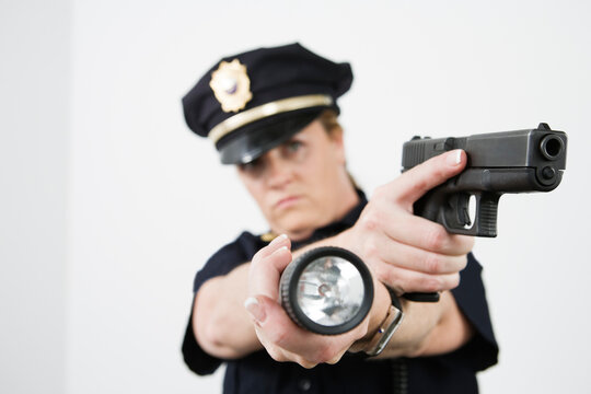 Police woman pointing handgun and holding flashlight.