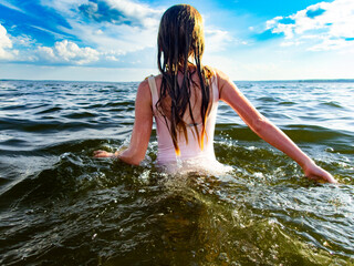 Young girl walks in ocean with blue sky and sunshine in swimsuit