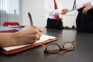 Person writing with business men shaking hands in the background.