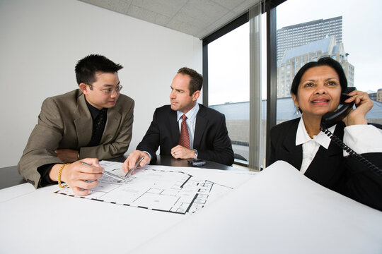View of businesspeople checking blueprint with a woman speaking on phone.