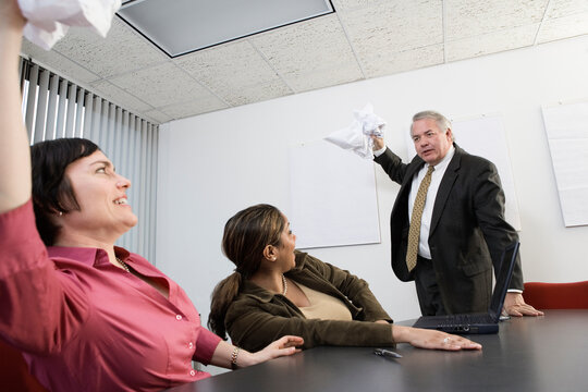 Business people throwing papers at each other in a conference room.