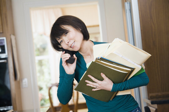Portrait of a mid adult woman holding a stack of files and talking on a mobile phone