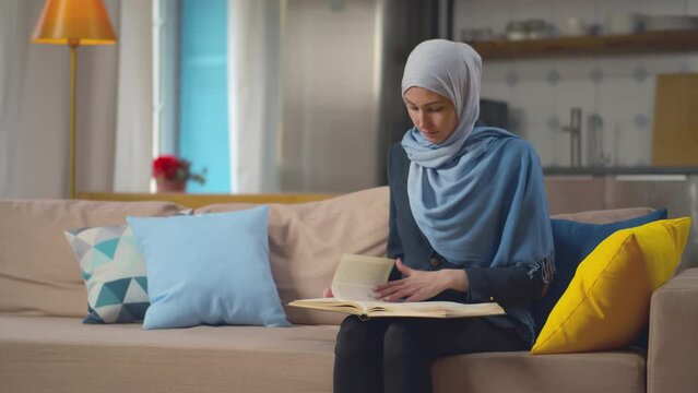 Muslim woman wearing hijab reading book at home. Realtime