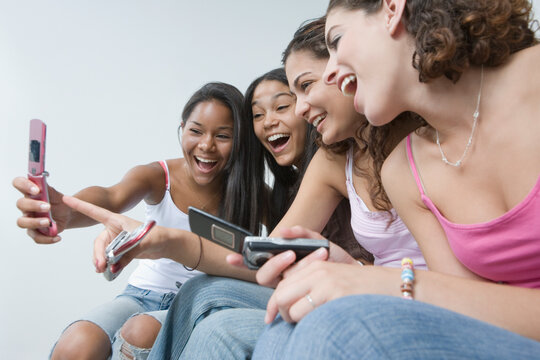 Four teenage girls looking at pictures on a mobile phone and smiling