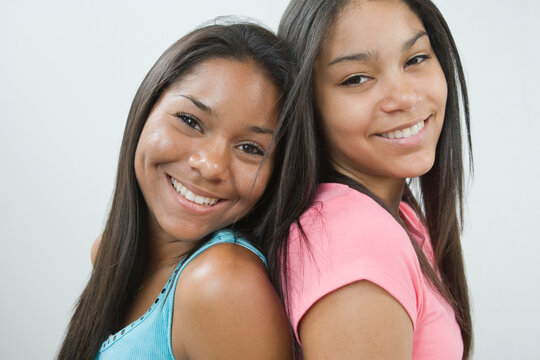 Portrait Of Two Teenage Girls Back To Back Smiling