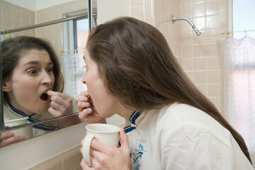 Side profile of a mid adult woman picking her teeth in the bathroom
