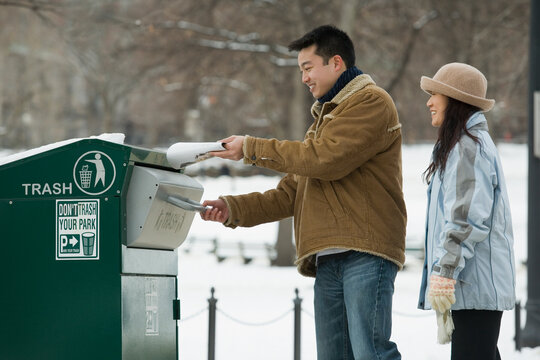 Young man throwing garbage into a garbage bin with a young woman standing behind him