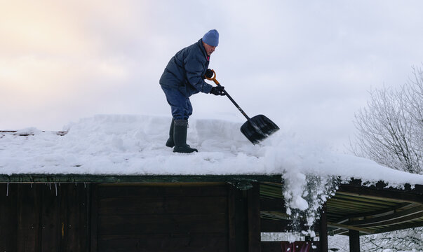 Man in action on the private house roof with shovel cleaning snow. Danger job.