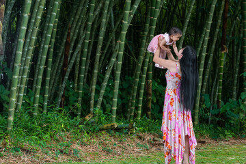 latin mother lifting her baby with her arms up, playing with the child in the middle of a bamboo forest.