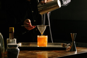 male bartender pouring a cocktail with a cocktail shaker straining into a rocks glass