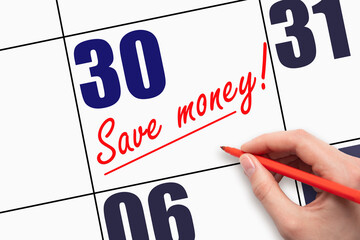 30th day of the month. Hand writing text SAVE MONEY and drawing a line on calendar date.