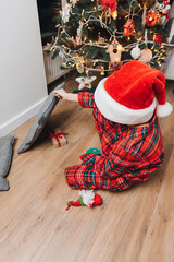 Obraz premium A boy in red pajamas near the Christmas tree is looking for a gift. Christmas at home. Family comfort. Front view