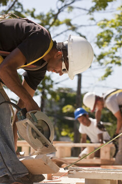 Carpenters using circular saw at a construction site with gable frame in the background