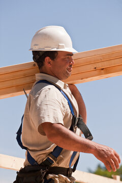 Carpenter carrying wall studs at a construction site