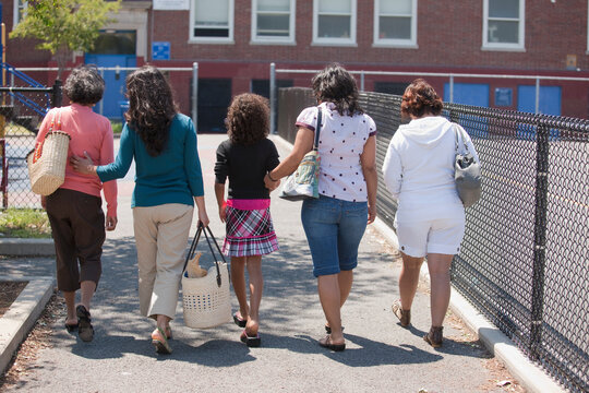 A group of women over three generations walking together in a row down an outdoor walkway
