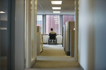 Rear view of a man sitting in a wheelchair in an office