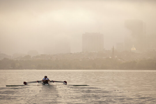 Person rowing a boat in a foggy river with city in the background, Charles River, Massachusetts State Capitol, Beacon Hill, Boston, Massachusetts, USA
