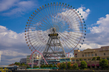Fototapeta premium This image features a large ferris wheel in Japan with a cloudy blue sky in the background.