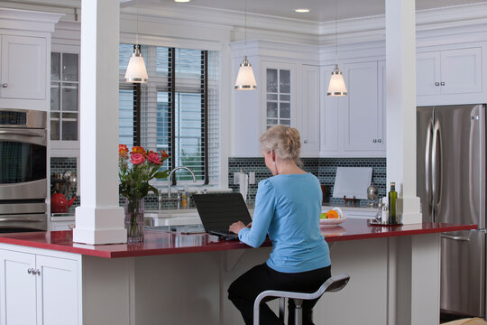 Woman on laptop in kitchen of a Green Technology Home with energy efficiency appliances, stone countertops, and recycled wood
