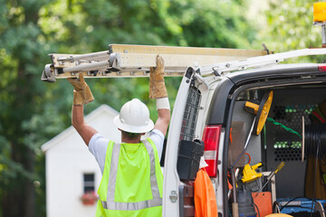 Communications worker loading a ladder onto a truck