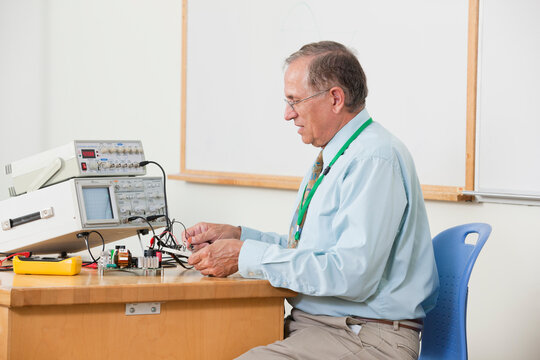 Professor wiring oscilloscope connections in electronics classroom
