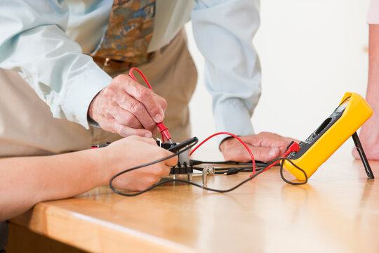 Engineering professor assisting student with multimeter measurement on circuit board