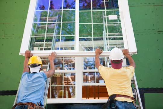 Carpenters positioning a large window frame on a house under construction