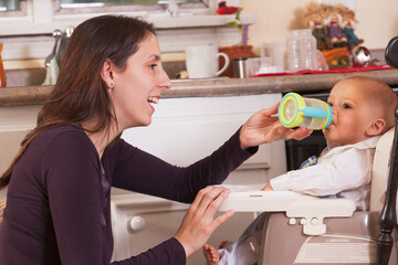 Mother feeding her son drinking from sippy cup