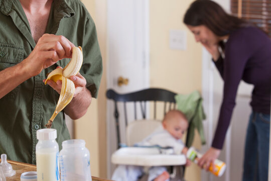 Mother feeding her son while father peeling a banana