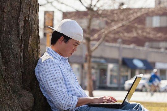 Chinese student sitting under a tree using laptop