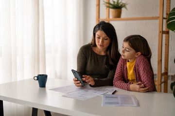 Mother going through her financials with her daughter...Young Caucasian mother going through her financials while sitting at home desk with her daughter.